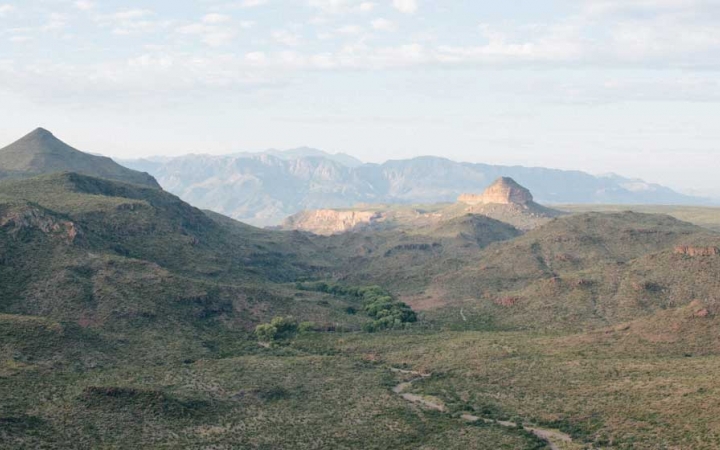 a river winds through a mountainous desert landscape dotted with green shrubs